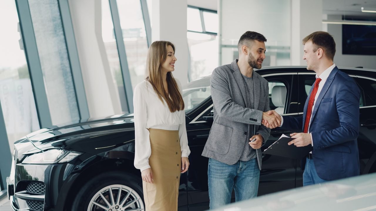 Customers shaking hands with dealer in showroom, sealing car purchase deal.