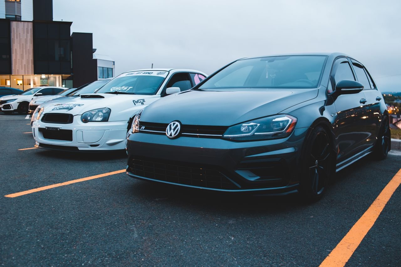 Modern black car with white racing automobile on city parking lot near contemporary building in twilight